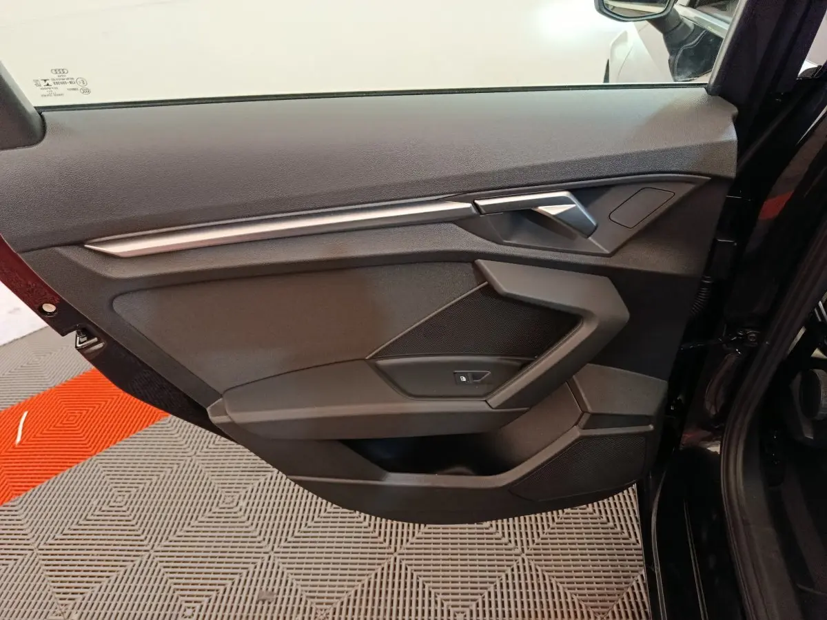 Porte intérieure côté gauche noire de l'Audi A3 30 TFSI MHEV 2022 avec poignée argentée et commande de vitre.