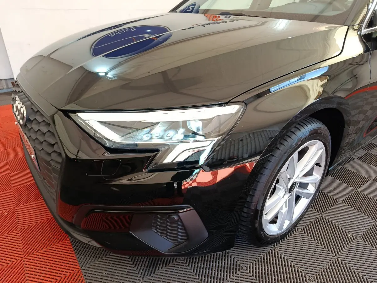 Vue 3/4 avant droit d'une Audi A3 noire mettant en valeur son phare LED et sa calandre distinctive.