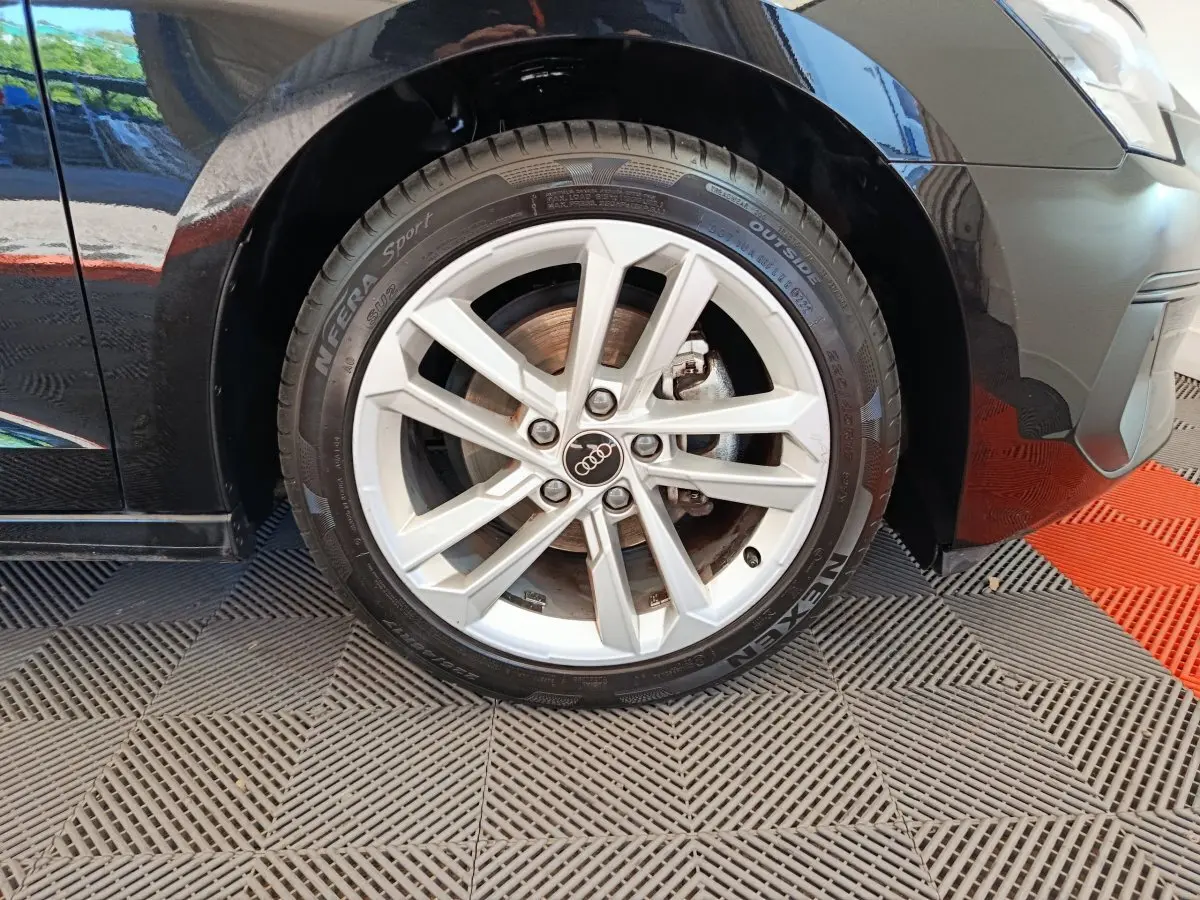 Gros plan sur la roue avant gauche noire d'une Audi A3 30 TFSI MHEV avec jante argentée à 5 branches doubles.