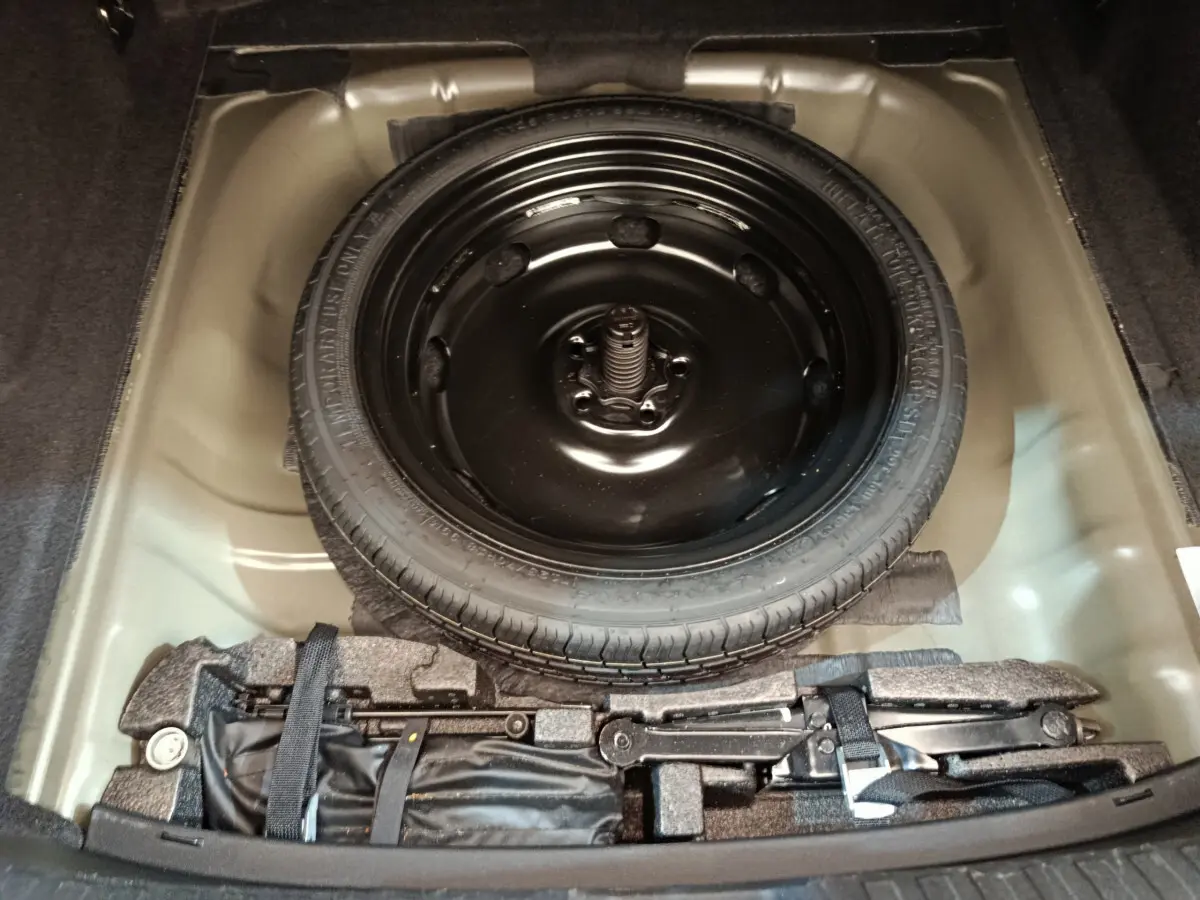 Vue plongeante sur la roue de secours noire et le coffre à outils dans le compartiment arrière d'une Audi A3 noire 2022.