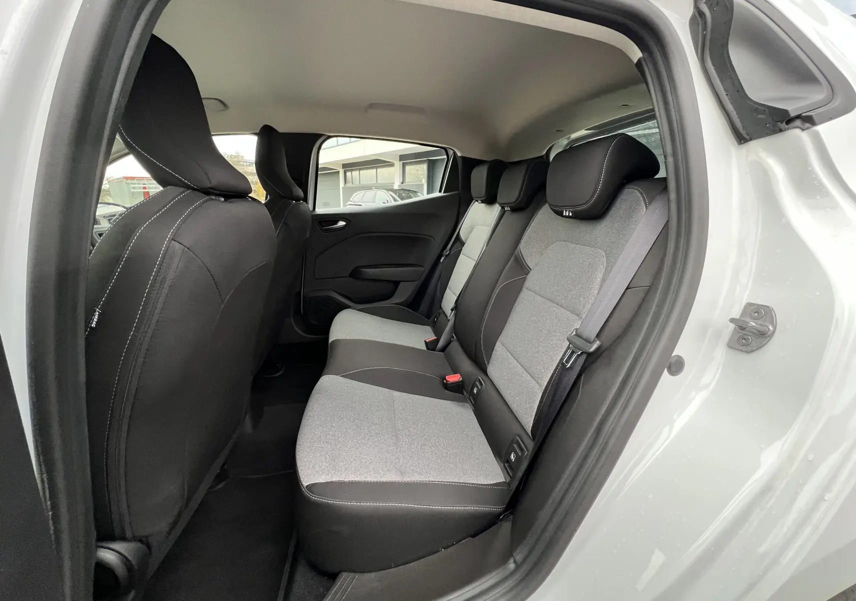 Vue intérieure arrière droite de la Renault Clio V blanche, sièges tissu gris avec appuie-têtes noirs contrastés.