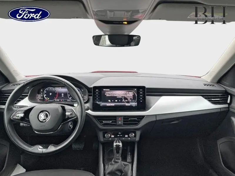 Vue intérieure avant du Skoda Kamiq rouge Velvet, tableau de bord moderne avec écran tactile central et volant multifonction.