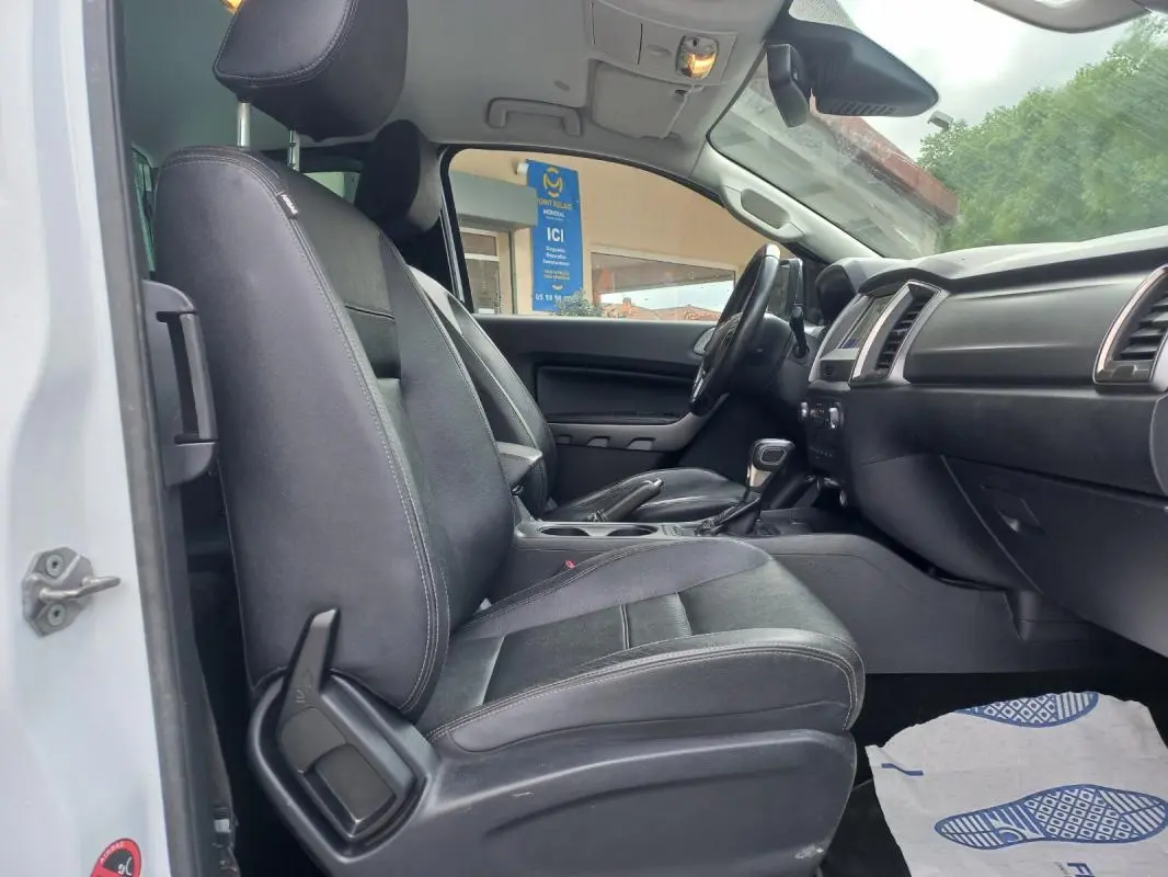Vue intérieure côté conducteur du Ford Ranger Super Cabine Limited 2022 blanc, sièges noirs en tissu et tableau de bord visible.