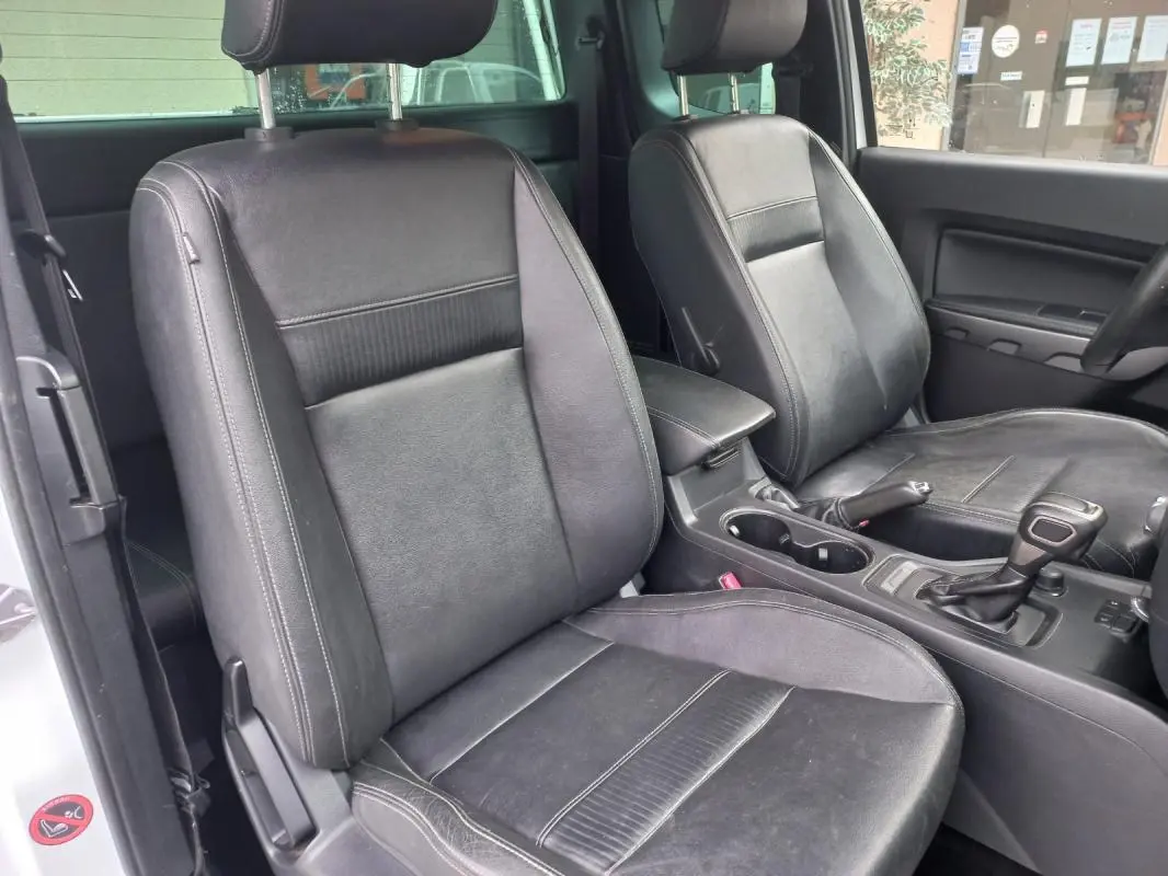 Vue intérieure du Ford Ranger 2022 en blanc, montrant les sièges avant en cuir noir et la console centrale avec levier de vitesse automatique.