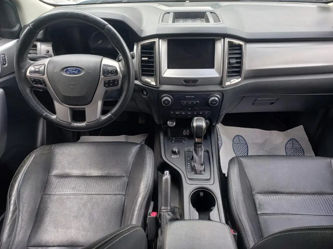 Vue intérieure avant du Ford Ranger 2022, tableau de bord et sièges noirs, volant multifonction et console centrale avec boîte auto.