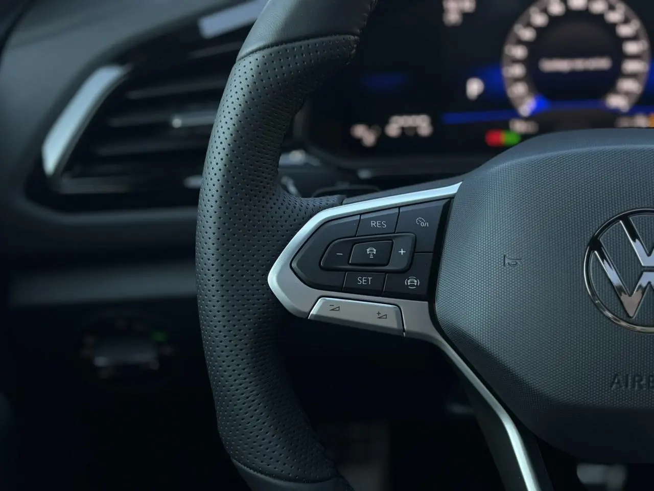 Gros plan sur le volant cuir perforé du Volkswagen T-Roc 2025 avec commandes multifonctions et logo VW central.