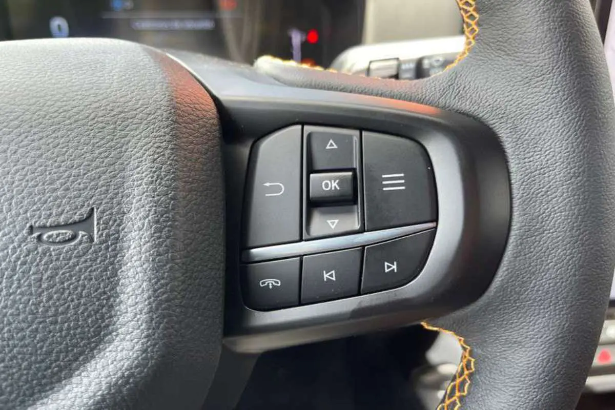 Gros plan sur les commandes multifonctions à droite du volant noir avec surpiqûres orange du Ford Ranger Wildtrak Plus 2025.