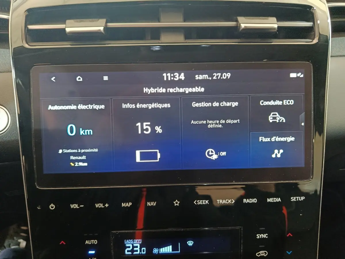 Écran tactile central du Hyundai Tucson marron affichant l'autonomie électrique et gestion de charge en vue frontale rapprochée.