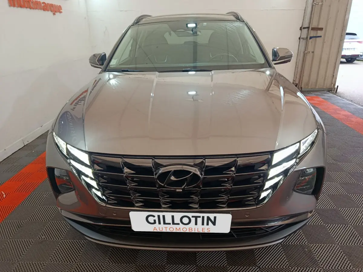 Vue avant d'un Hyundai Tucson marron 2022 avec calandre noire brillante et phares LED allumés.