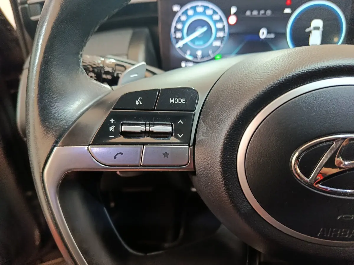 Gros plan sur le côté gauche du volant noir du Hyundai Tucson 2022, avec commandes audio et affichage digital en arrière-plan.
