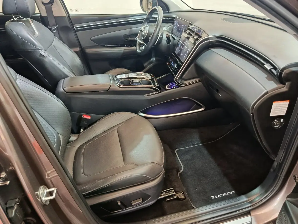 Intérieur avant droit du Hyundai Tucson marron 2022 avec sièges cuir noirs et tableau de bord tactile lumineux.
