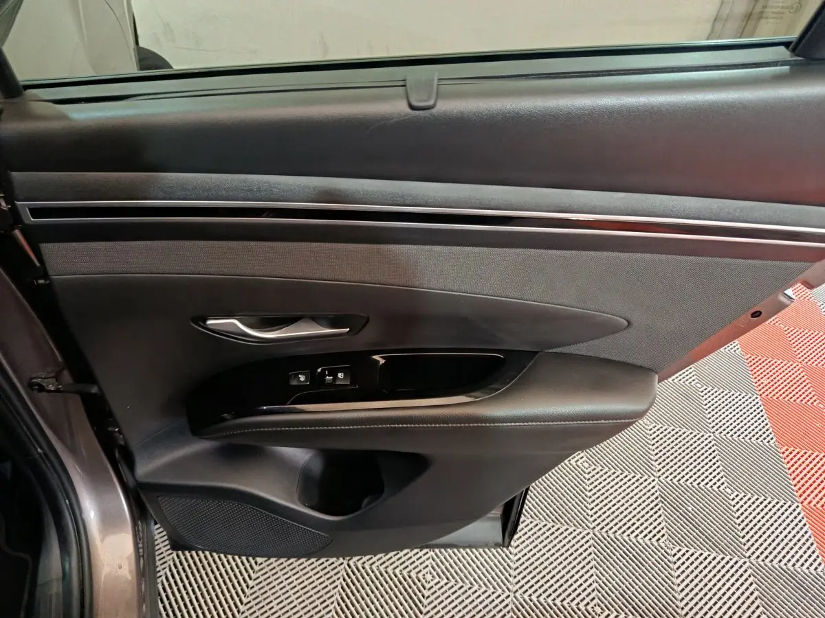 Vue intérieure côté gauche de la porte avant du Hyundai Tucson marron, avec commandes de vitres et poignée argentée.