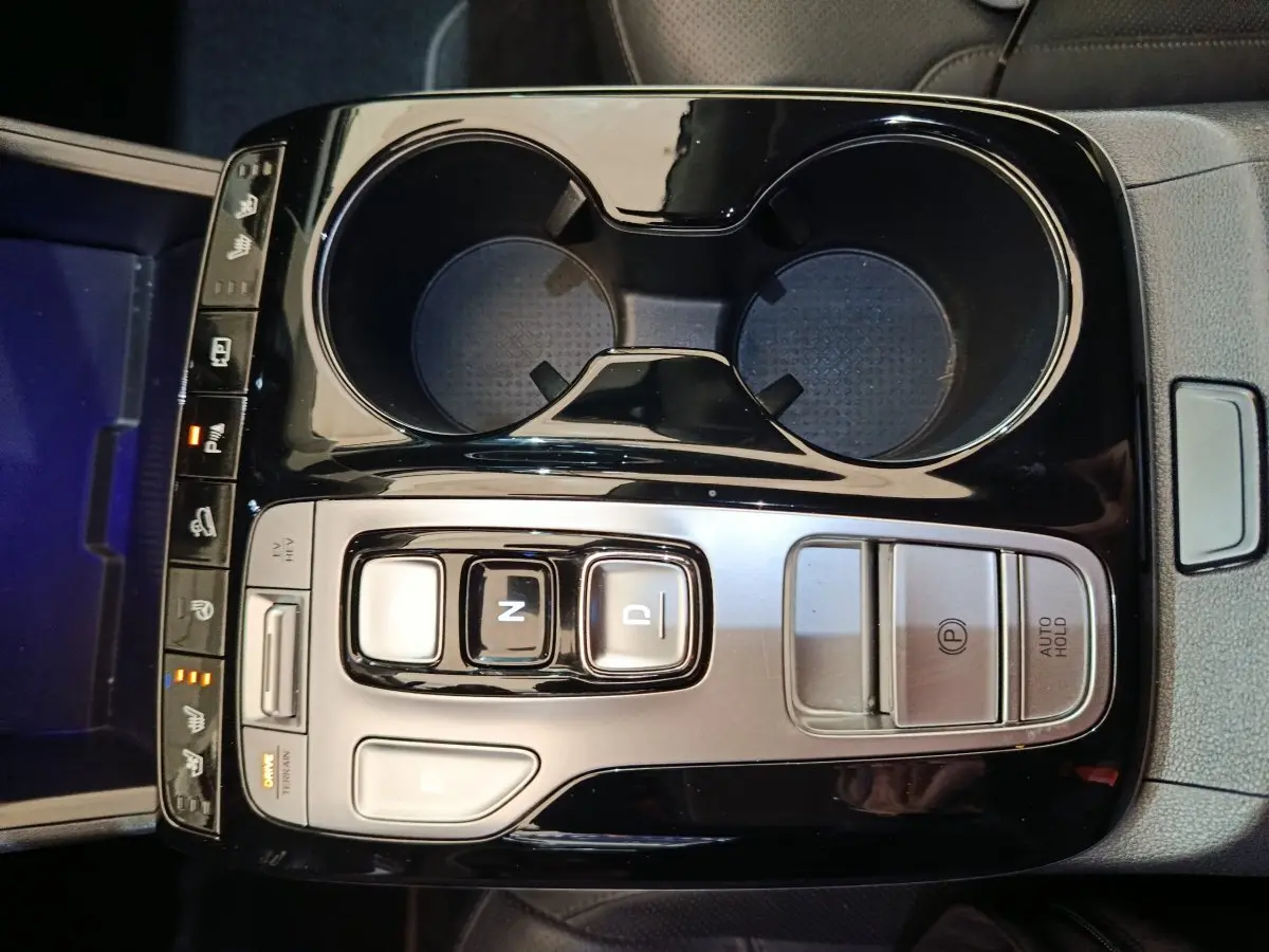 Vue plongeante sur la console centrale noire et argentée du Hyundai Tucson marron, avec commandes de boîte auto et porte-gobelets.