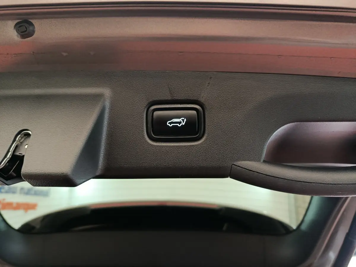 Bouton d'ouverture électrique du coffre sur la trappe intérieure d'un Hyundai Tucson marron 2022 hybride rechargeable.