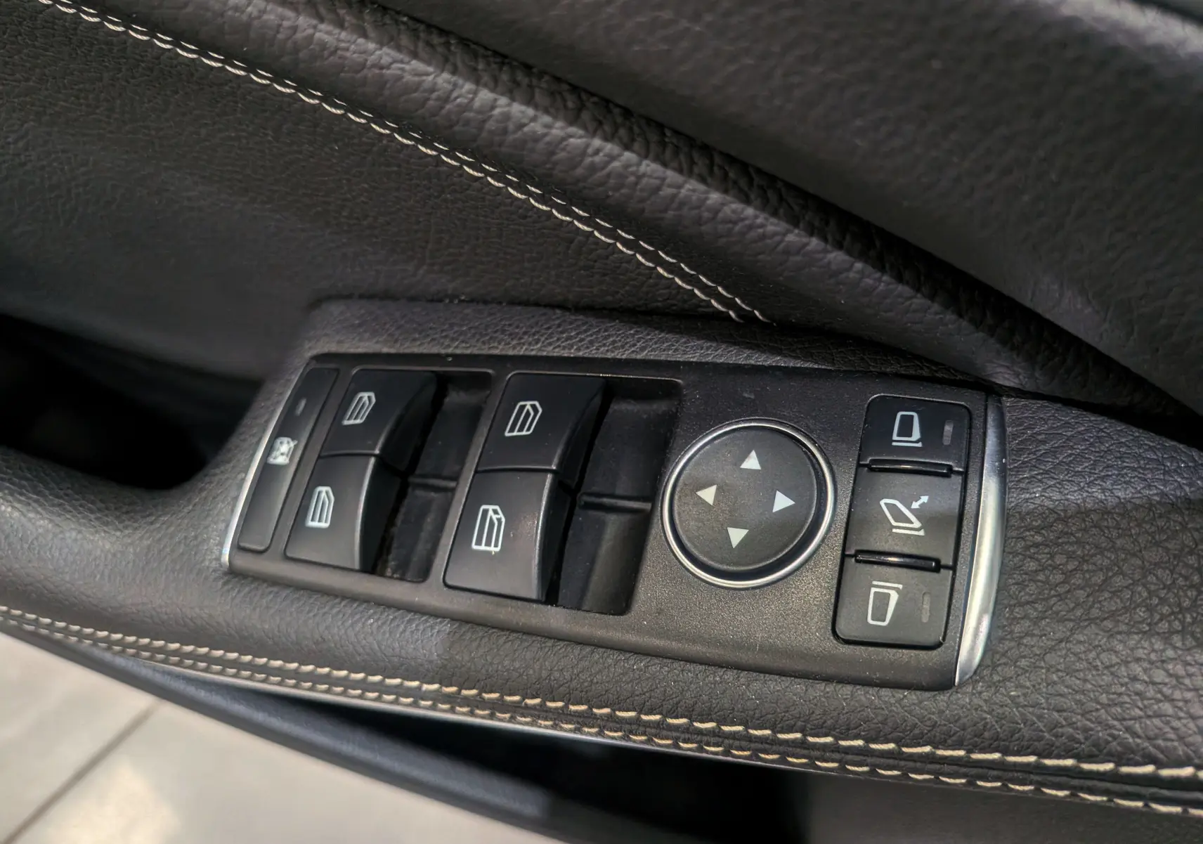 Gros plan sur les commandes de lève-vitres et réglage des rétroviseurs côté gauche d'une Mercedes Classe A blanche.