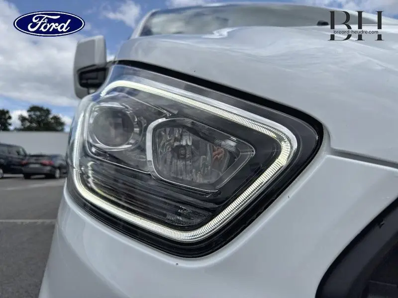 Gros plan sur le phare avant gauche du Ford Transit Custom blanc Glacier, mettant en valeur son éclairage LED distinctif.