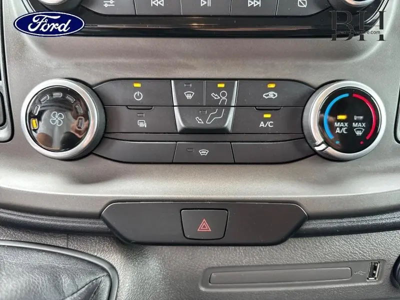 Détail du tableau de bord du Ford Transit Custom blanc, montrant les commandes de climatisation et le bouton de warning.