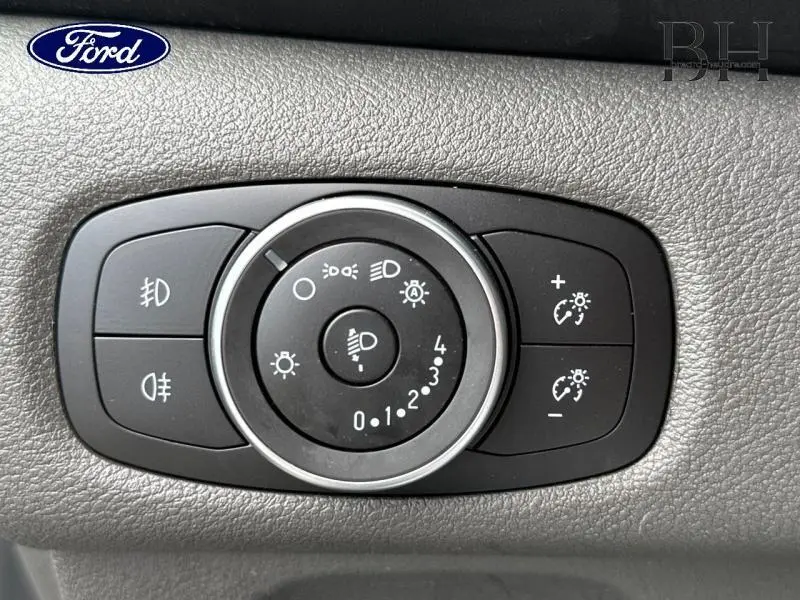 Gros plan sur le panneau de commande des phares du Ford Transit Custom blanc, avec réglages d'intensité et feux antibrouillard.