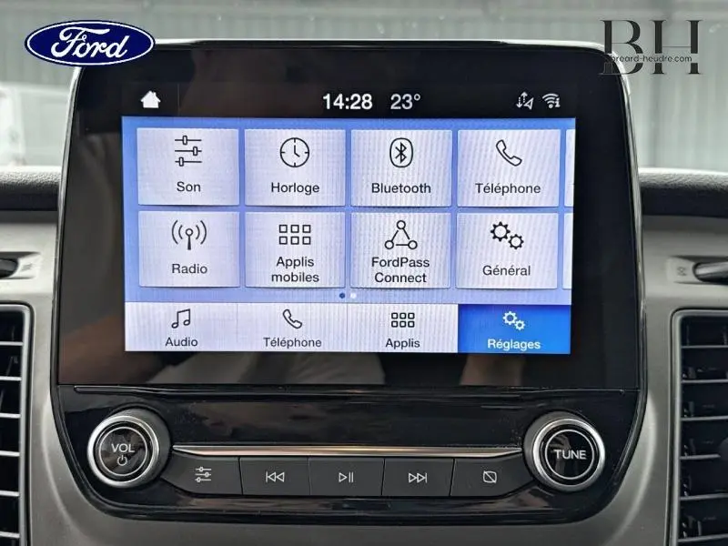 Écran tactile central du Ford Transit Custom blanc, affichant le menu principal du système multimédia avec commandes audio en dessous.