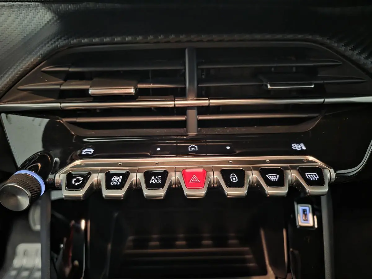 Gros plan sur la rangée de boutons de commande sous la sortie d'air centrale du tableau de bord noir brillant du Peugeot 2008 gris.