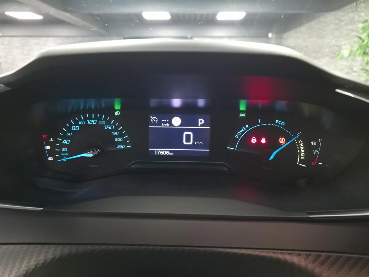 Vue rapprochée du tableau de bord numérique du Peugeot 2008 gris, affichant la vitesse à 0 km/h et l'autonomie hybride.