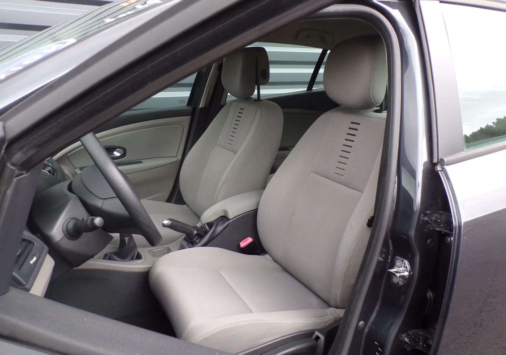 Vue intérieure côté conducteur d'une Renault Mégane III Expression DCI 85 anthracite bleuté avec sièges tissu gris clair.