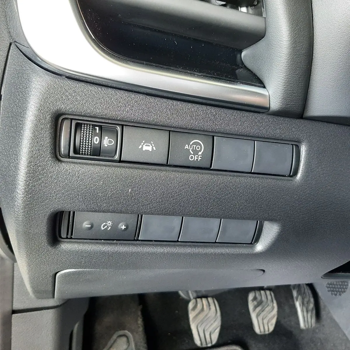 Vue du tableau de bord côté gauche d'un Nissan Qashqai blanc lunaire 2022, avec commandes d'assistance et pédales visibles.