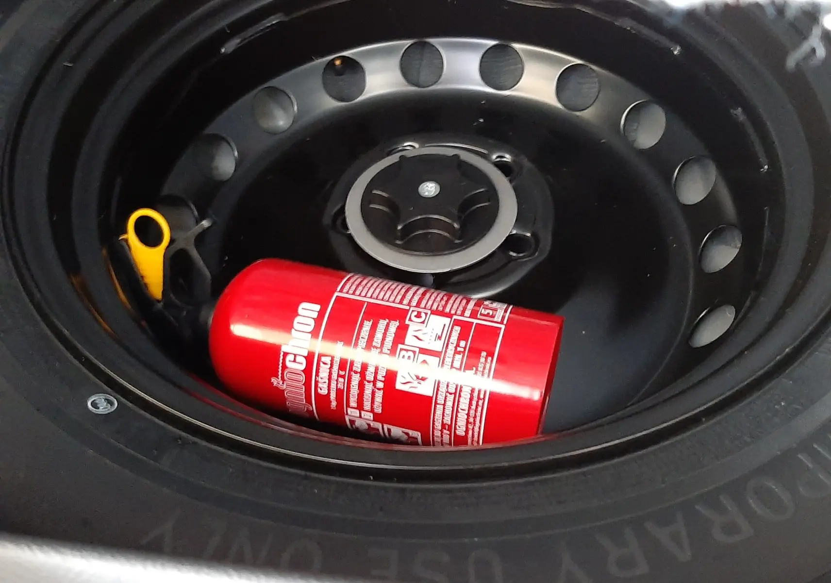 Gros plan sur la roue de secours noire d'un Nissan Qashqai blanc lunaire avec un extincteur rouge posé à l'intérieur.