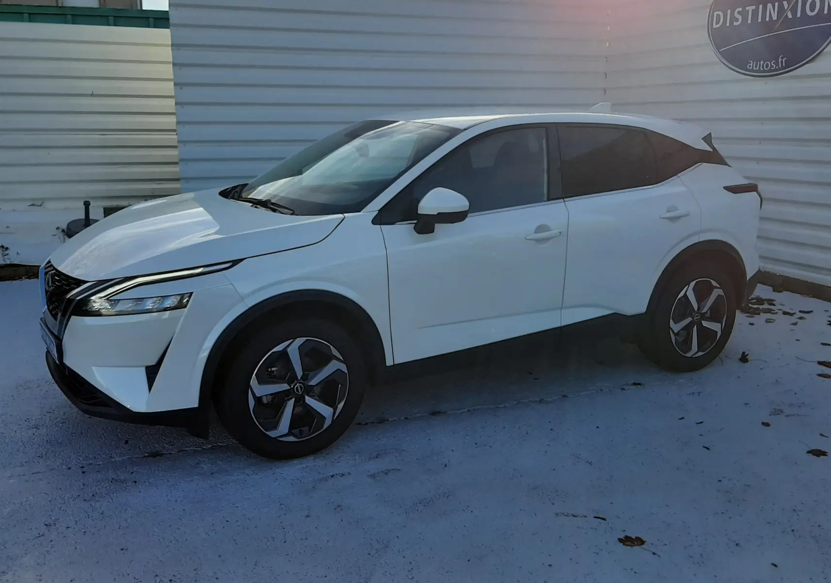 Nissan Qashqai blanc lunaire vu de profil côté gauche, avec jantes alliage et vitres teintées, stationné en extérieur.