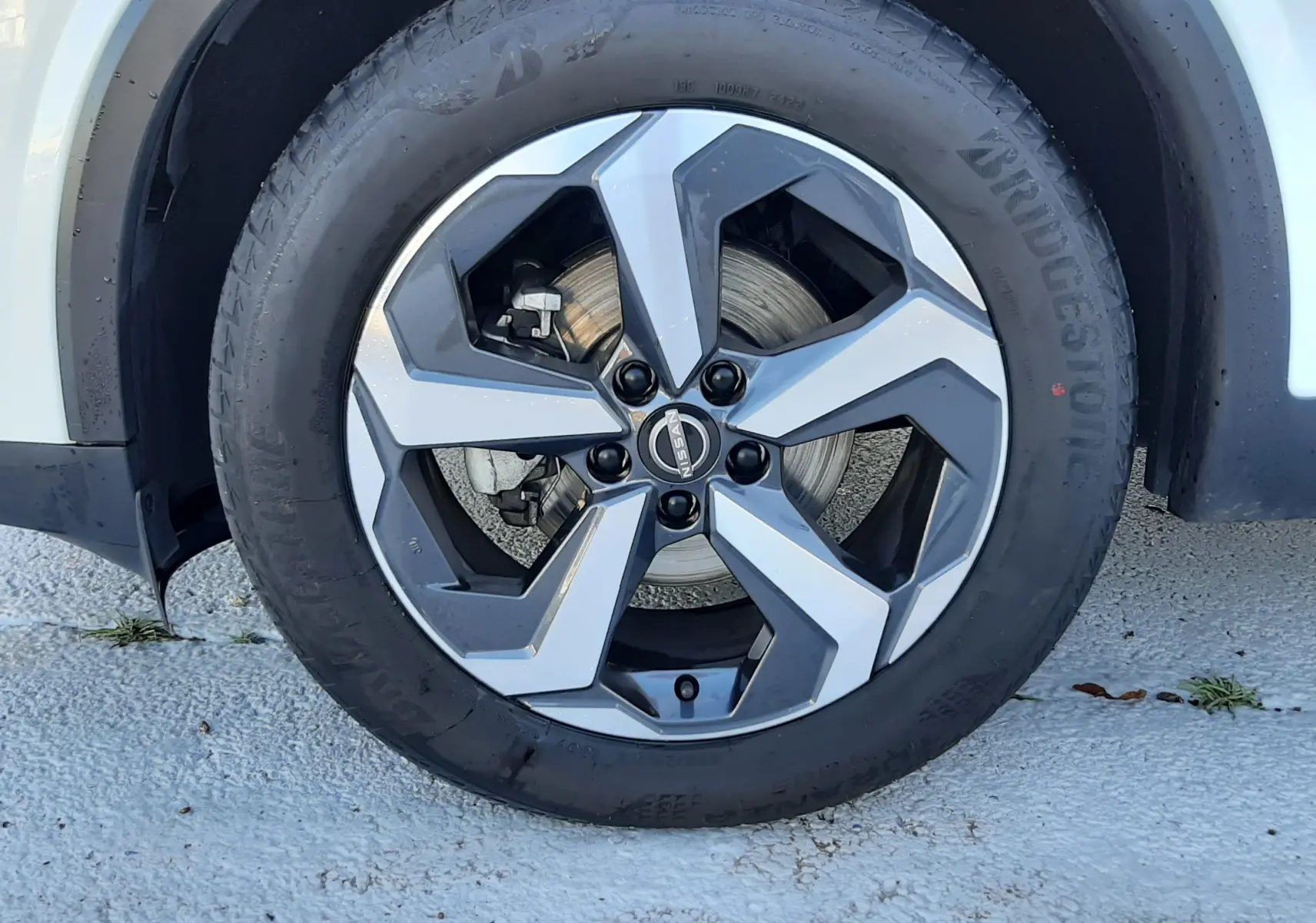 Gros plan sur la roue avant droite d'un Nissan Qashqai blanc lunaire avec jante alliage au design moderne.