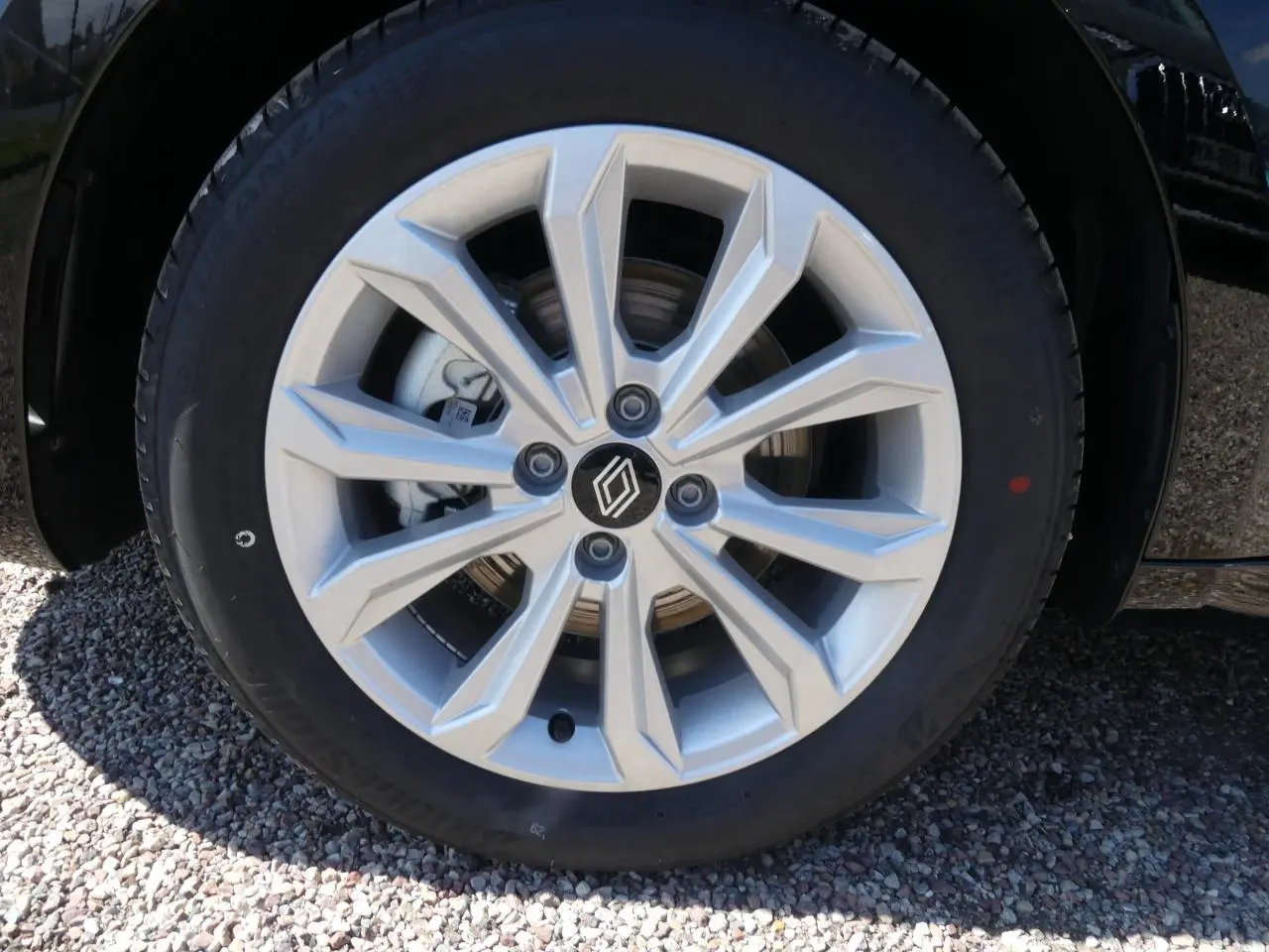 Gros plan sur la roue avant droite d'une Renault Clio noire métallisée avec jante argentée à motifs géométriques.