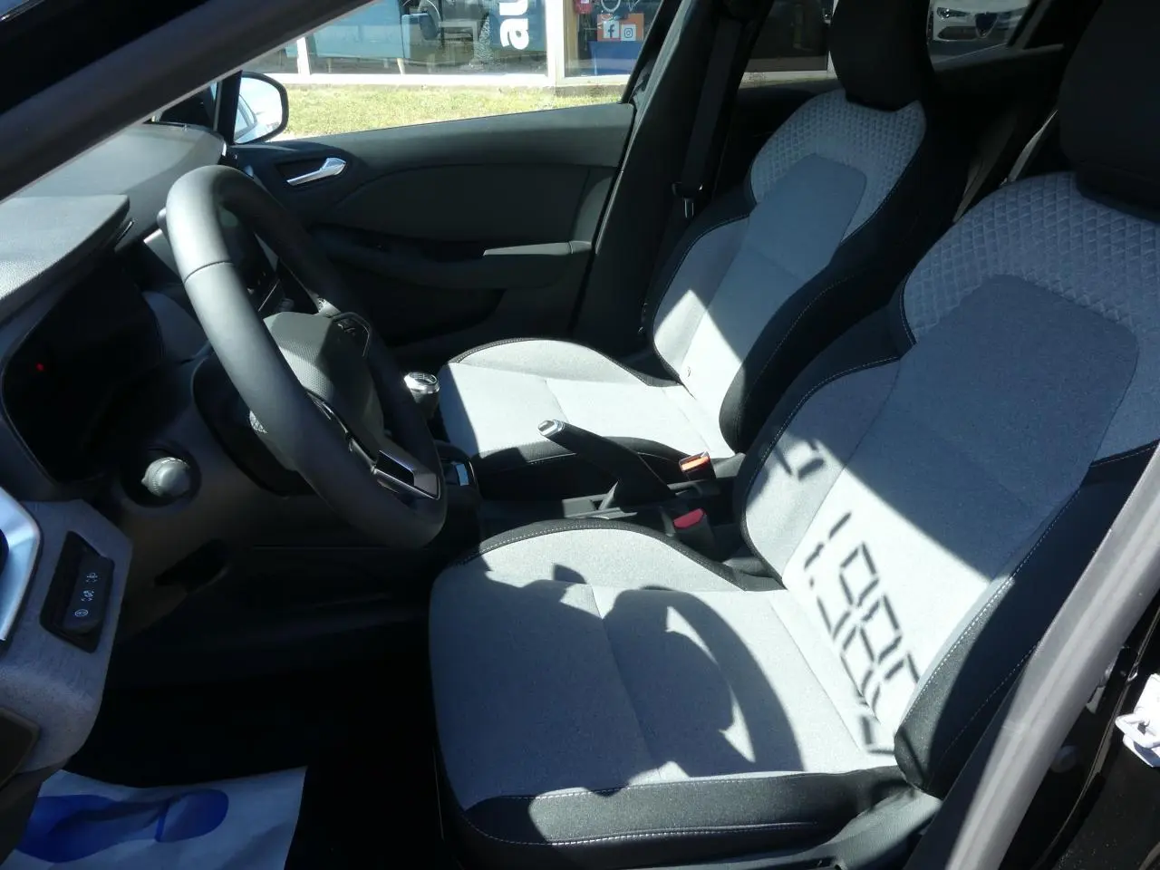 Intérieur avant droit de la Renault Clio 2025, sièges tissu gris avec motifs 3D et volant multifonction noir.