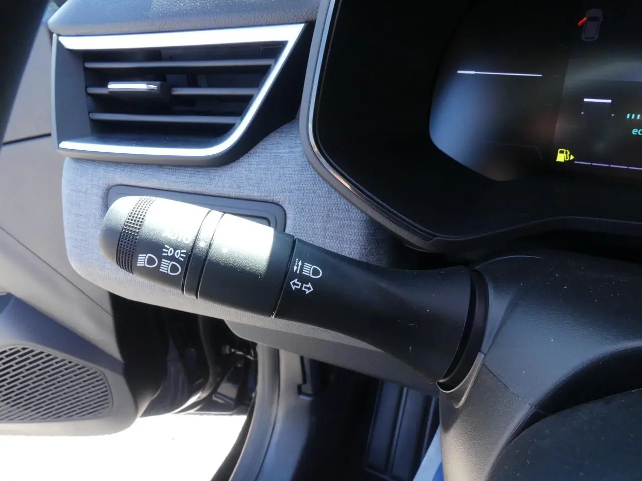 Gros plan sur la commande des feux et clignotants côté gauche du tableau de bord gris clair de la Renault Clio noire.