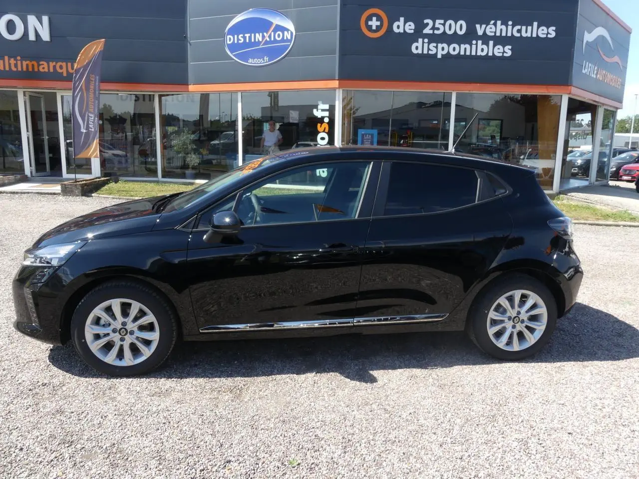 Profil côté gauche d'une Renault Clio noire métallisée avec jantes alliage et baguettes chromées visibles.