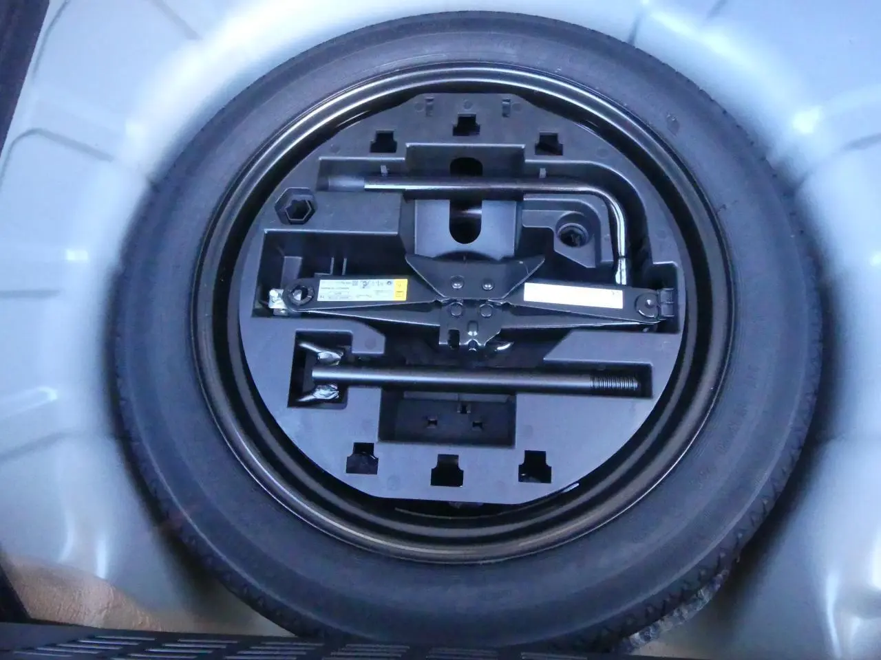 Roue de secours temporaire avec outillage intégré dans le coffre d'une Renault Clio noire métallisée 2025.