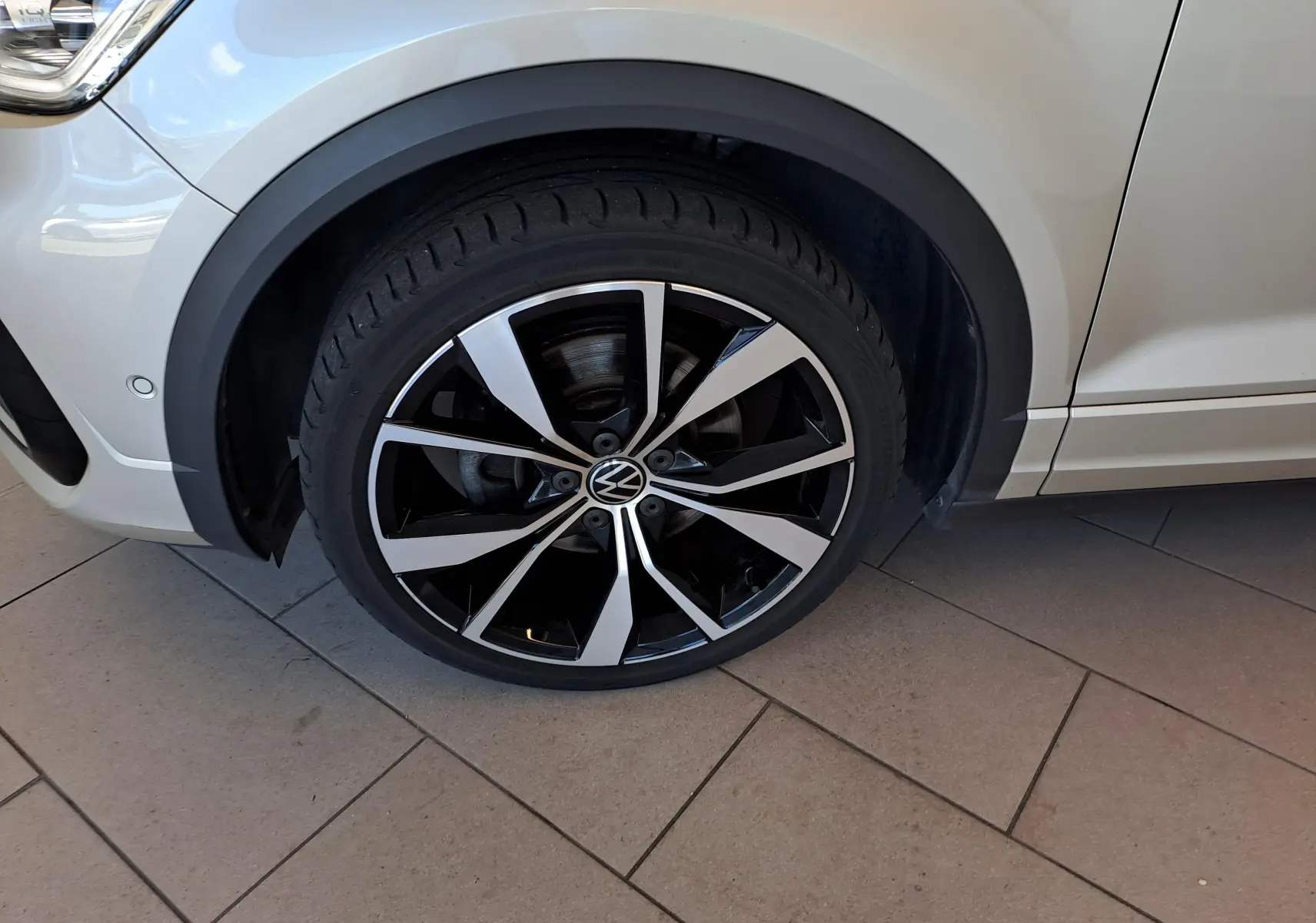 Gros plan sur la roue avant gauche du Volkswagen T-Roc Cabriolet gris ivoire avec jante alliage 19'' Misano noire et argentée.