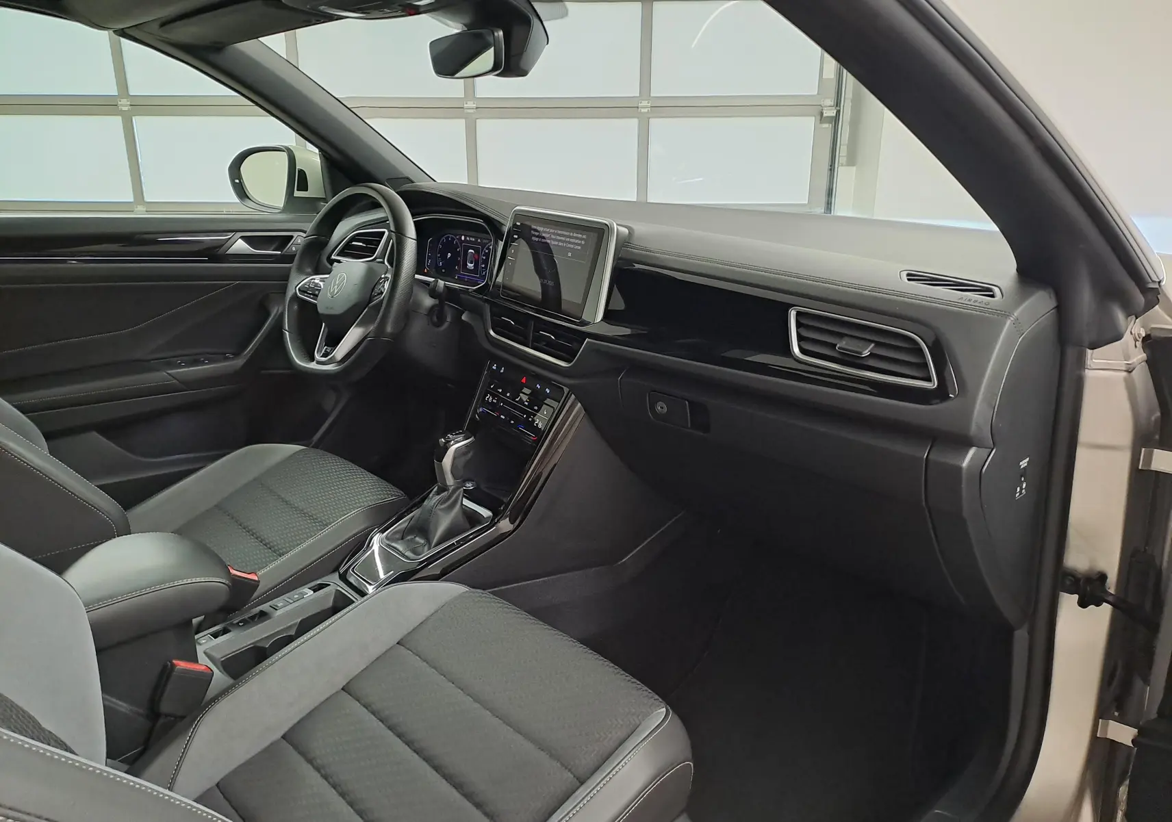 Intérieur côté conducteur du Volkswagen T-Roc Cabriolet gris ivoire, tableau de bord moderne avec écran tactile central.