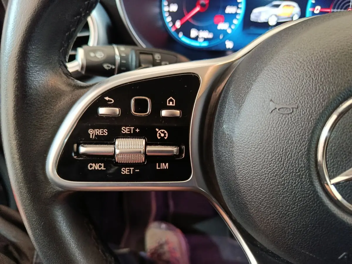 Gros plan sur les commandes du volant cuir noir du Mercedes GLC 300 e Business Line 4Matic, avec tableau de bord numérique en arrière-plan.