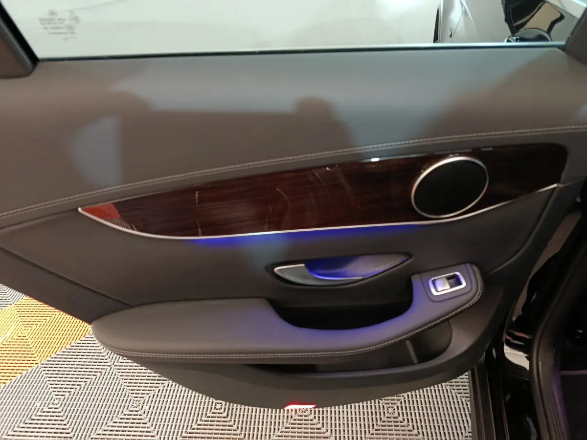 Gros plan sur la porte côté gauche du Mercedes GLC 300 e Business Line 2020, garniture bois et éclairage d'ambiance bleu.