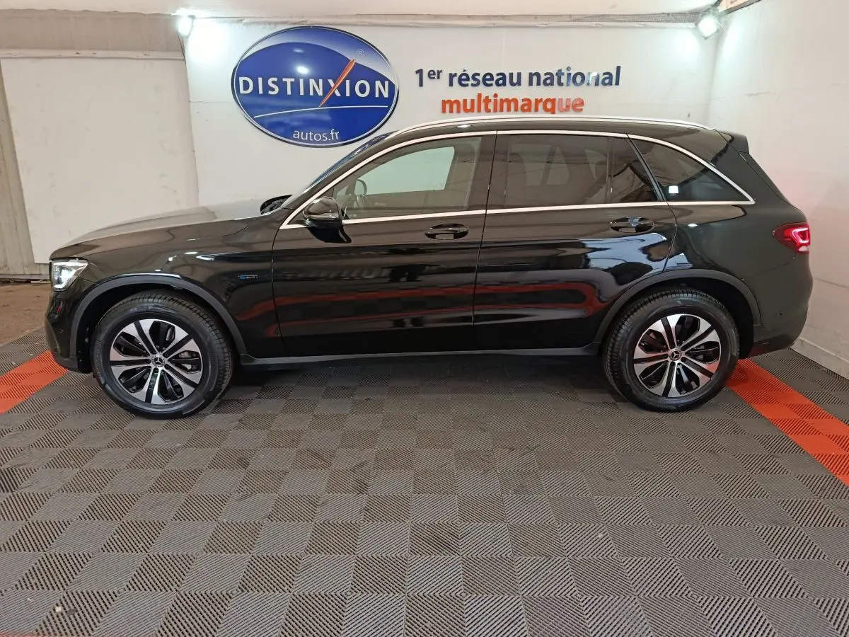 Profil côté gauche d'un Mercedes GLC 300 e Business Line noir, hybride rechargeable, sur sol damier en intérieur showroom.
