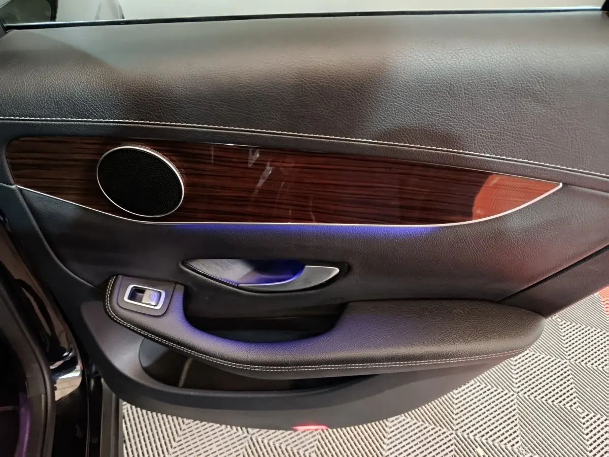 Vue intérieure côté gauche de la porte noire du Mercedes GLC 300 e Business Line avec garniture bois et éclairage d'ambiance bleu