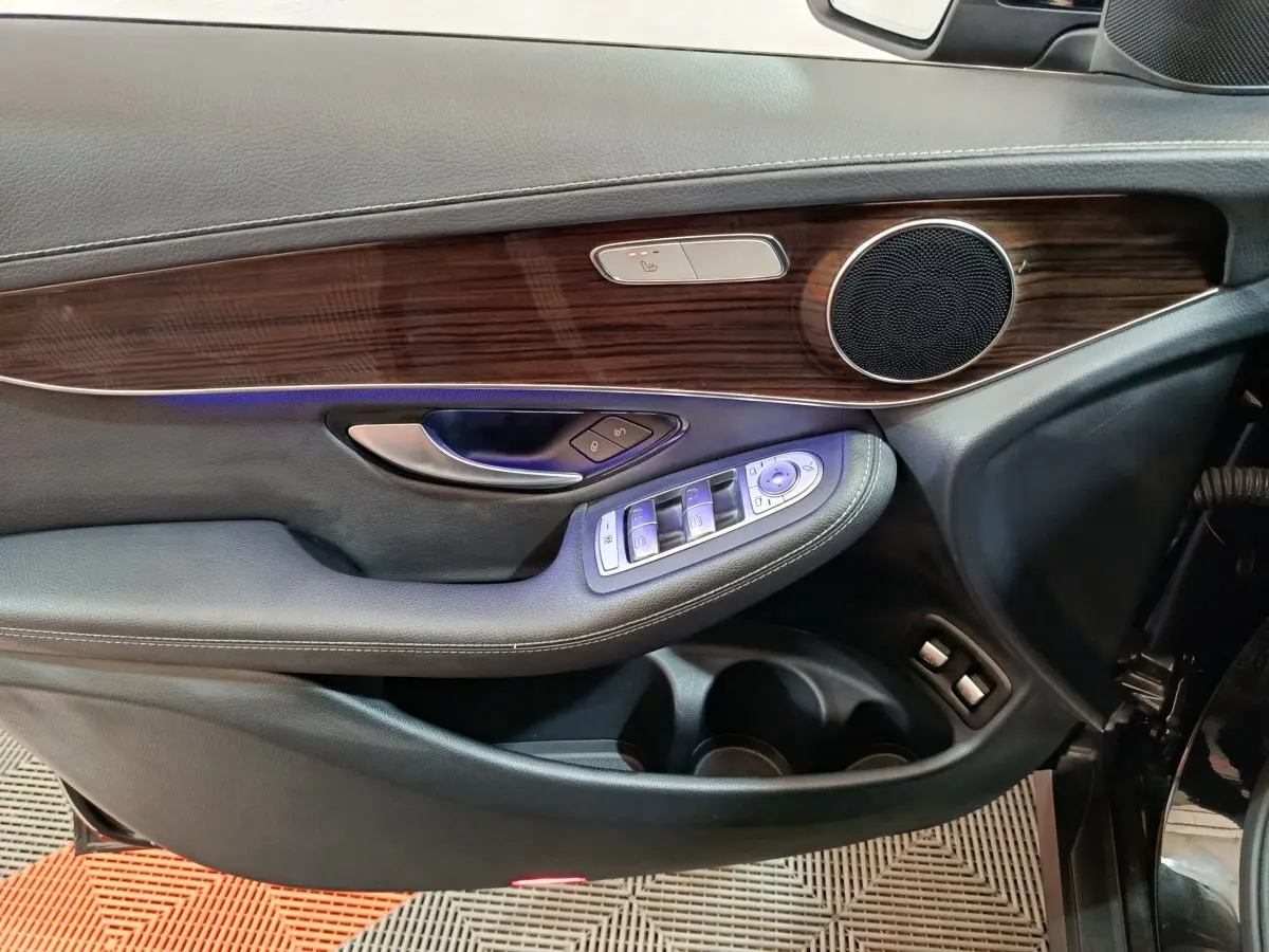 Gros plan sur la porte avant gauche noire du Mercedes GLC 300 e Business Line avec garniture bois et commandes électriques.