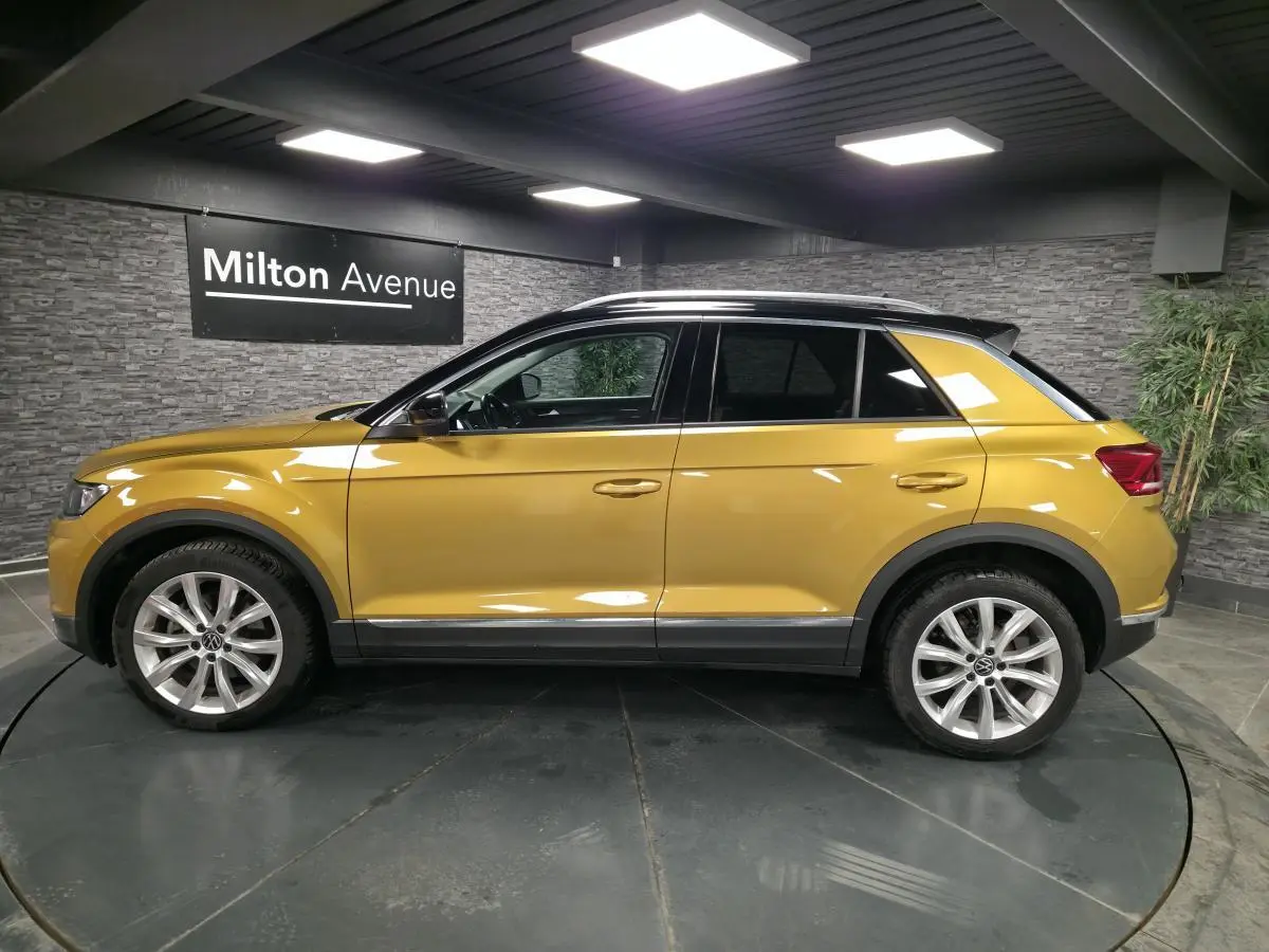 Volkswagen T-Roc jaune Curcuma vu de profil côté gauche avec toit noir et jantes alliage 18 pouces.