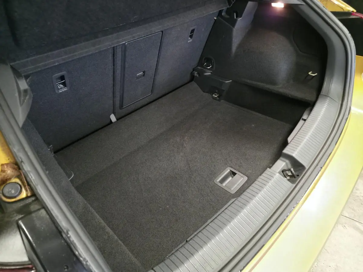 Coffre ouvert vu de dessus du Volkswagen T-Roc orange, montrant l'espace de rangement vide et la moquette noire.