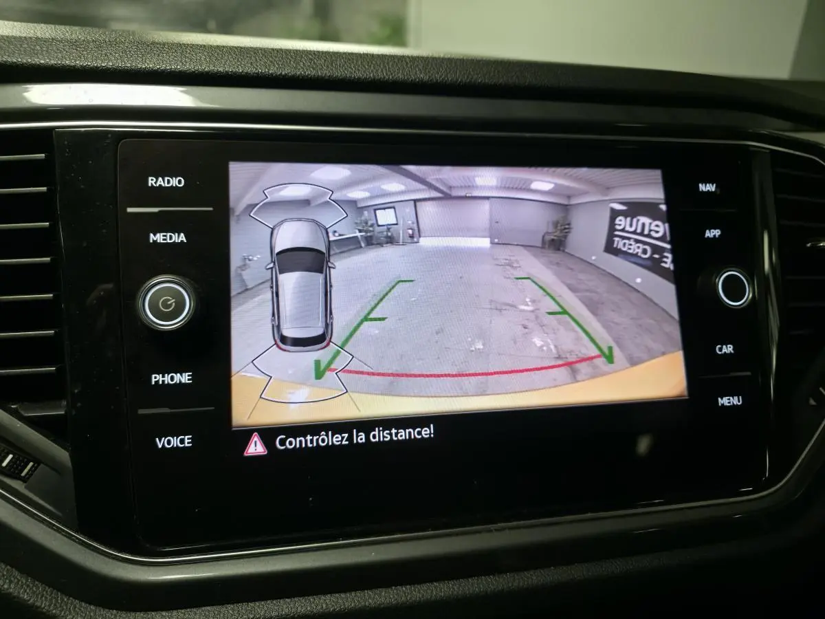 Écran tactile de la Volkswagen T-Roc affichant la caméra de recul avec alertes de distance en intérieur de garage.