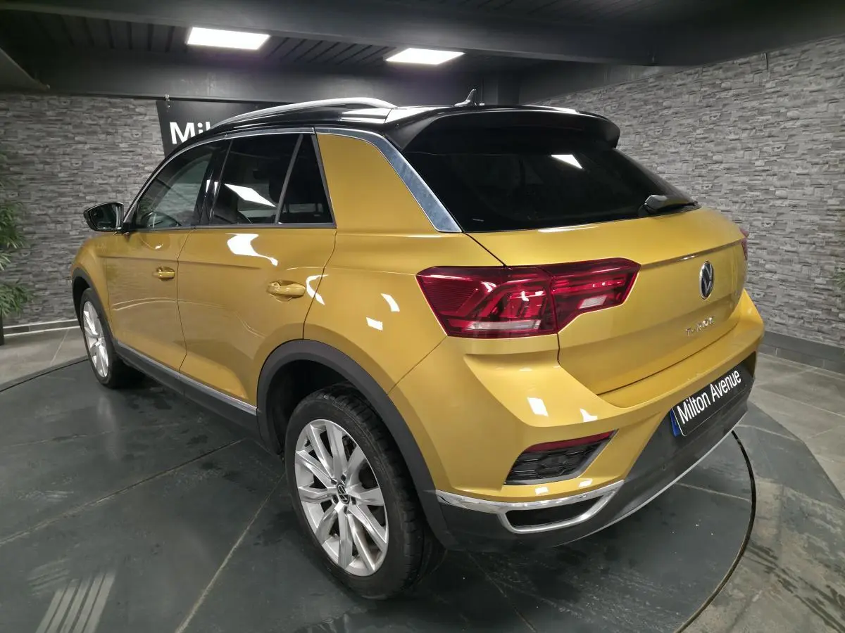 Vue 3/4 arrière droite d'un Volkswagen T-Roc jaune Curcuma avec toit noir et jantes alliage 18 pouces.