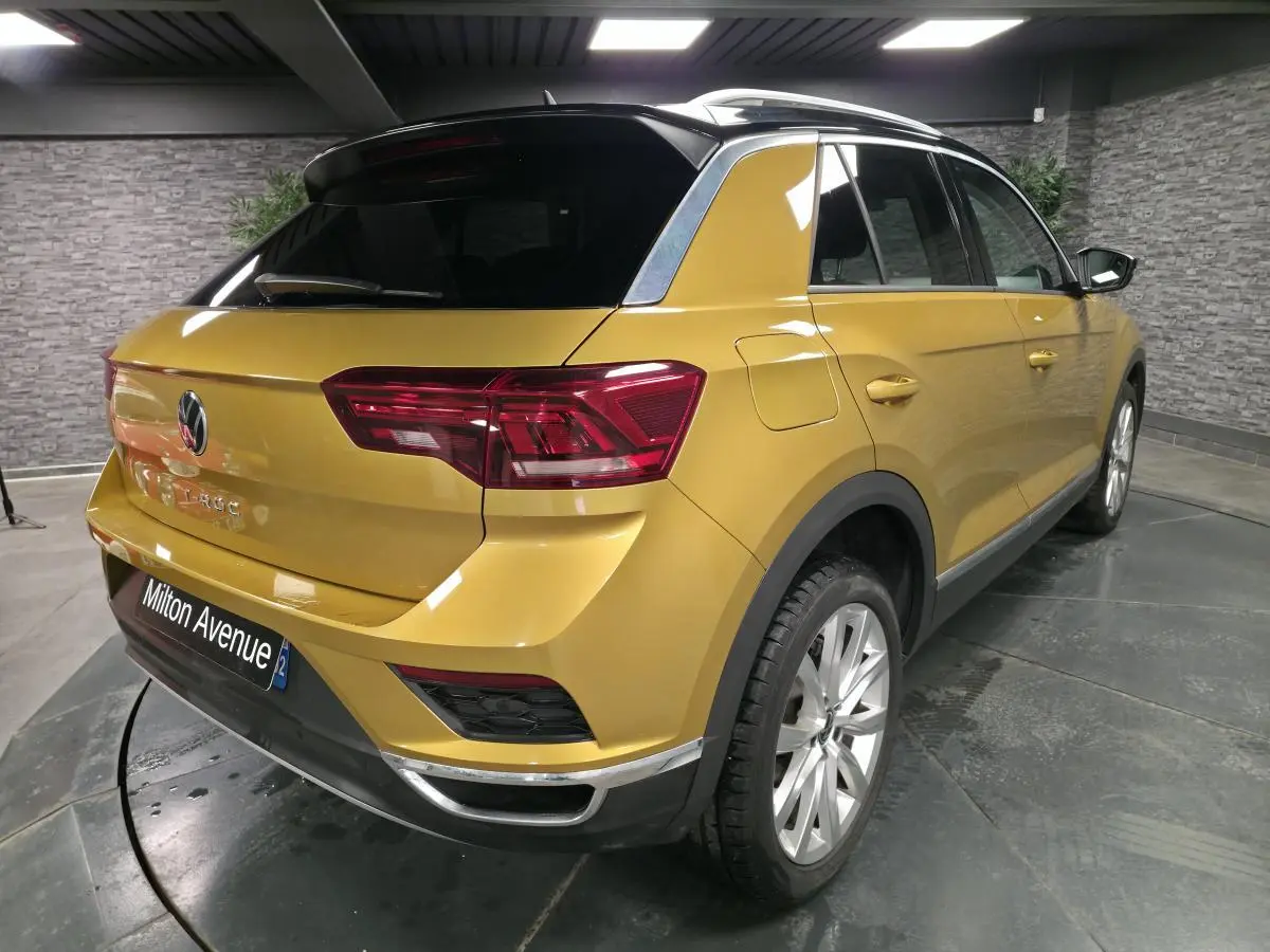 Vue 3/4 arrière droite d'un Volkswagen T-Roc jaune Curcuma avec toit noir et jantes alliage 18 pouces.