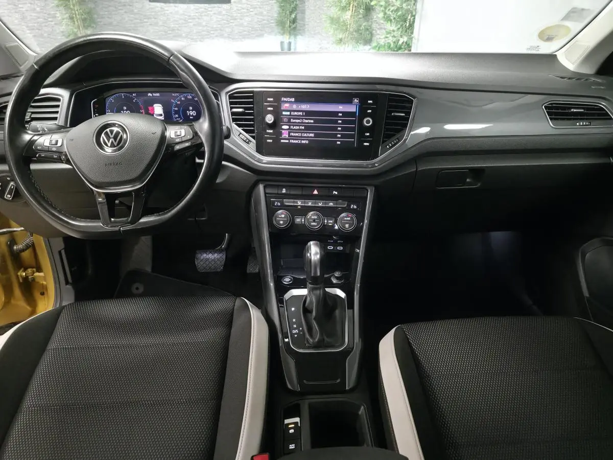 Vue intérieure avant du Volkswagen T-Roc 2021, tableau de bord noir avec écran tactile et volant multifonction cuir.