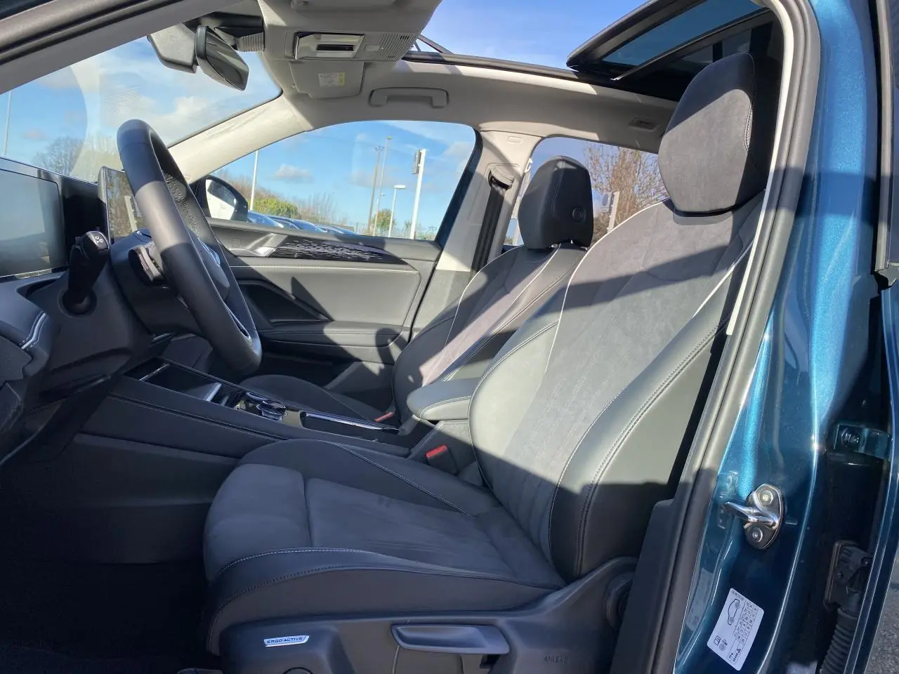 Intérieur du Volkswagen Tiguan 2025 en Nightshade Blue, vue côté gauche sur les sièges avant en microfleece et toit ouvrant panoramique.