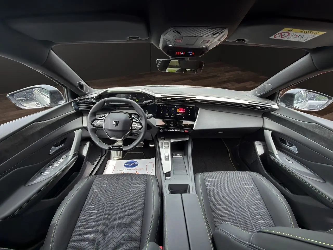 Vue intérieure avant de la Peugeot 308 GT 2026, tableau de bord moderne avec volant compact et sièges tissu noir.